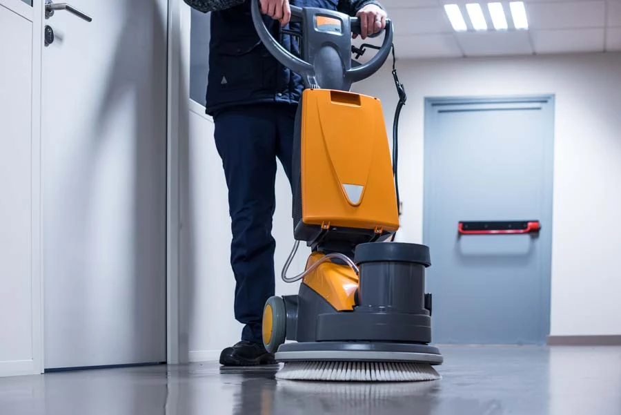 Employé en tenue de travail utilisant une monobrosse professionnelle sur sol carrelé dans un hall d'immeuble moderne